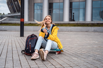 Beautiful girl calls by phone and sits on skateboard.