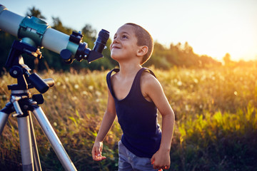 Little boy using telescope in nature to explore the universe.