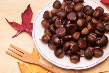 plate of chestnuts on wooden background and leaves
