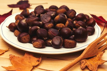 plate of chestnuts on wooden background and leaves
