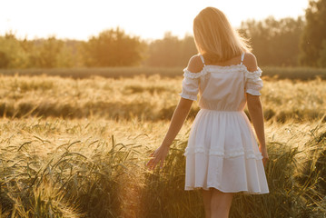 Beauty Girl Outdoors enjoying nature. Beautiful Teenage Model girl in white dress running on the Spring Field, Sun Light.