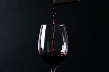 Fototapeta na wymiar Tasty sweet red wine pouring into tha wineglass against black background