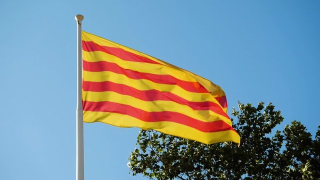 Close-up shot of the flag of Catalonia waving in the wind against blue sky. Barcelona. Spain. Slow motion. HD