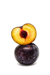 A red plum and half of the plum on top of it on white background