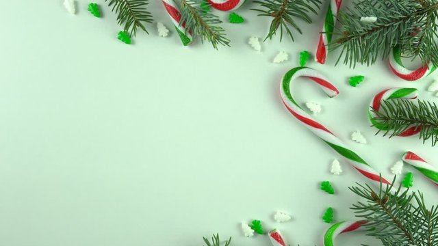 Loop of Christmas season day table still frame, close up with various candy canes and holiday sweets arranged on white background. New year decoration with various sprinkles and fir, pine branches.