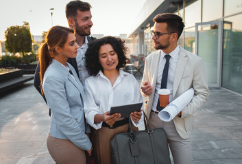 Fototapeta premium Group of coworkers standing outside in front of office buildings discuss about business plan and looking at tablet.