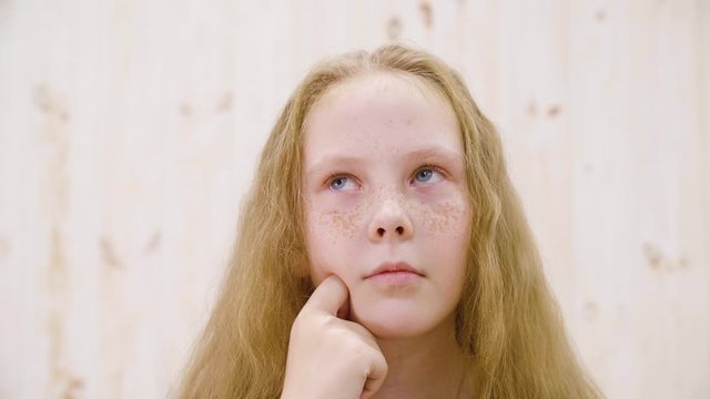 Portrait red haired thoughtful girl with freckles looking thoughtfully in light studio. Close up face thinking girl teenager looking up. Facial emotions concept