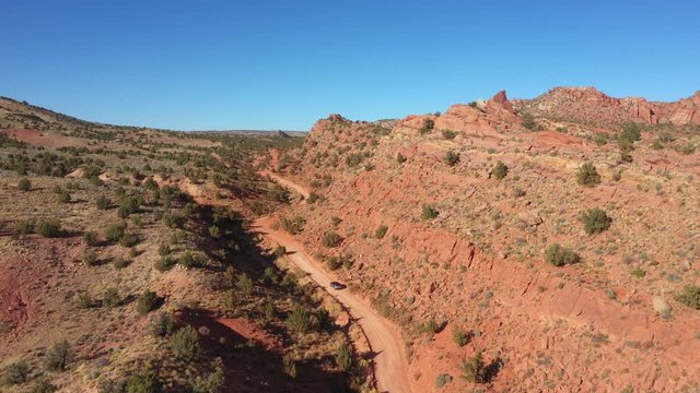 Dark SUV Drives On Dirt Road Crossing A Red Sand Desert With Rocks On Sunny Day