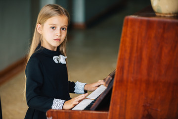 Little girl in a black dress learns to play the piano. The child plays a musical instrument.