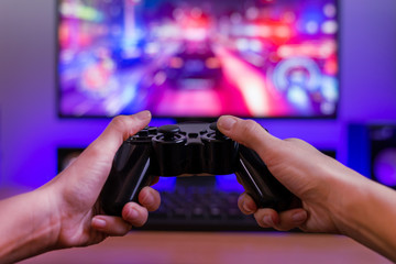 Joypad in hands. Gaming concept. Computer display with racing game and rgb light in background.