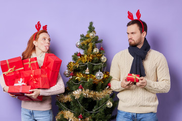 Cheerful pretty sister getting many boxes with christmas gifts, teasing handsome brother with small...