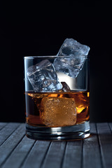 glass of whiskey with ice on a wooden surface