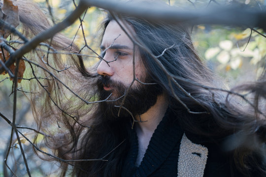 atmospheric autumn outdoor portrait of young man wearing long hair, beard and moustache, standing between trees