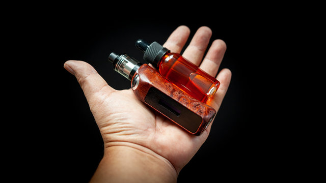 rebuildable tank atomizer with high end stabilized redwood burl regulated box mods and e-liquid bottle  in hand on black background, vaping device, selective focus