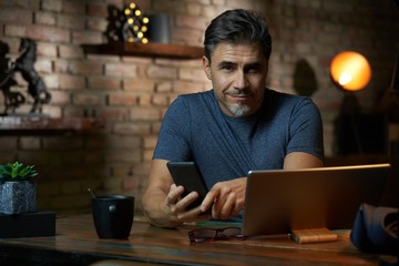 Older man sitting at desk using phone and tablet