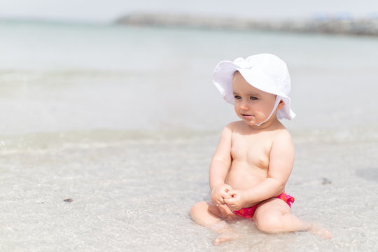 Baby girl looking straight ahead whilst sitting in the shallow sea waters