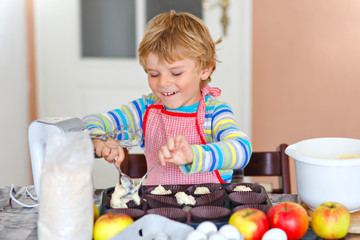 Cute little happy blond preschool kid boy baking apple cake and muffins in domestic kitchen. Funny...