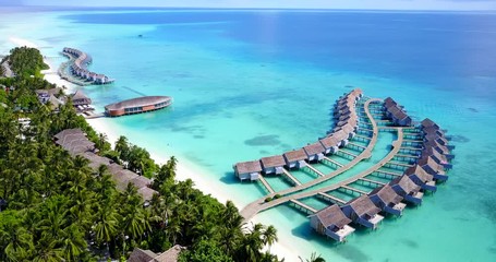 Aerial shot pan of a drone flying above a tropical island with crystal clear waters and an over water bungalow complex in Maldives - Powered by Adobe