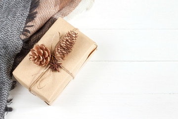Christmas box with a gift in craft paper, a scarf, a plaid, cones, anise on a white wooden background in a rustic style top view, copy space. New Year and Christmas concept