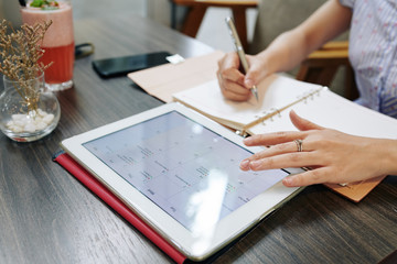 Businesswoman writing appointments in her planner when checking online calendar