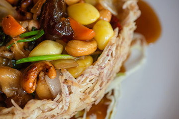 Sweet and sour stir-fried chicken with cashews, lotus seeds, Chinese gardenia, carrots, onions and vegetables topped with sauce in a bowl made with taro. It's a traditional Thai food.