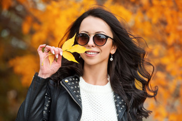 Beautiful woman walking outdoors in autumn. Smiling girl collects yellow leaves in autumn. Young woman enjoying autumn weather.