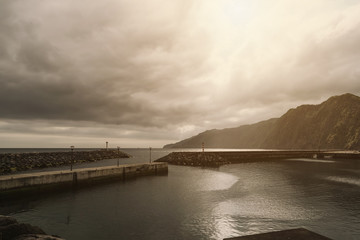 Obraz premium Wall separating Atlantic ocean from the area of a small port. Mountains in the background. Sao Miguel, Azores Islands, Portugal