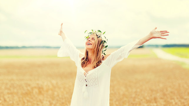 happiness, nature, summer holidays, vacation and people concept - smiling young woman in wreath of flowers and white dress on cereal field