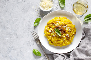 Traditional Italian risotto with mushrooms, saffron, parmesan cheese served with white wine on light background. Top view with copy space.