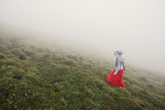 Woman wearing red dress and white hat walking in fog mountains