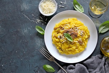 Traditional Italian risotto with mushrooms, saffron, parmesan cheese served with white wine on dark background. Top view with copy space.