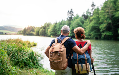 Rear view of senior tourist couple on a walk in nature, standing by lake. - Powered by Adobe