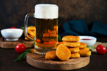 A mug of cold beer with foam with appetizer, chicken nuggets and sauce served on a wooden table.