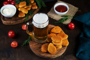 A mug of cold beer with foam with appetizer, chicken nuggets and sauce served on a wooden table.