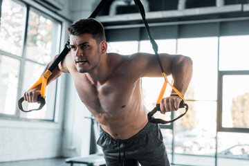handsome sportsman working out on suspension trainer in sports center