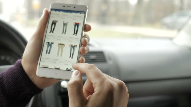 A man looks at the goods in the online clothing store, sitting in the car. Smart phone online shopping.