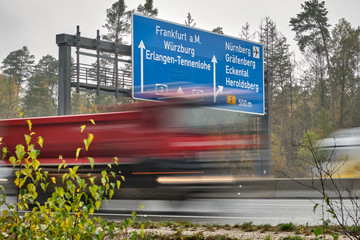 Fototapeta premium Trucks in blurred motion driving along signpost on highway A3 in Germany showing the way to Frankfurt am Main, Würzburg, Erlangen and Nürnberg. Seen on a wet and rainy November day near Nuremberg