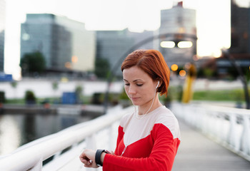Fototapeta premium Young woman with smartwatch on bridge outdoors in city, resting after exercise.
