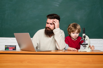 Teacher and kid. father teaching her son in classroom at school. Teacher helping young boy with lesson. Teacher helping pupils studying on desks in classroom. Teacher and child