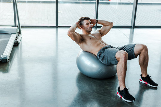 handsome sportsman doing crunches on fitness ball in sports center