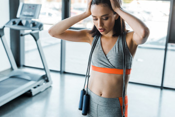 attractive sportswoman with skipping rope touching head in sports center