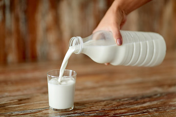 food, eating and dairy products concept - close up of female hand pouring milk from bottle to glass