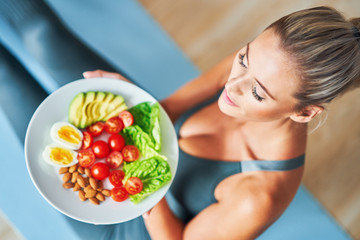 Adult woman eating healthy lunch and sitting on yoga mat