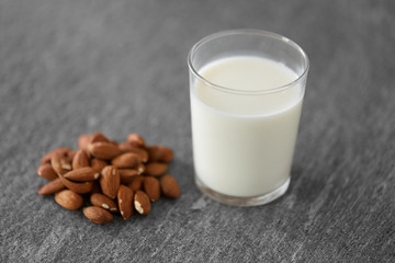food and dairy products concept - glass of lactose free milk and almonds on stone table