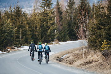 Obraz premium Rear view of mountain bikers riding on road in mountains outdoors in winter.