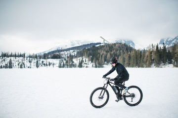 Side view of mountain biker riding in snow outdoors in winter nature.