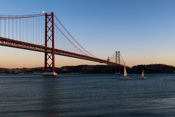 Sailing boats in the Tagus River passing by the 25 of April Bridge (Ponte 25 de Abril), in the city of Lisbon, Portugal; Concept for travel in Portugal