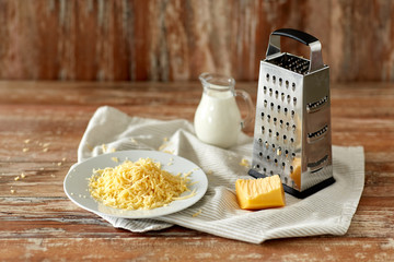 food, cooking and eating concept - close up of grated cheese, grater and jug of milk on wooden table