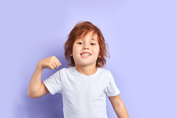 Portrait of caucasian child wearing white t-shirt shows how he is strong and powerful, idolated over purple background