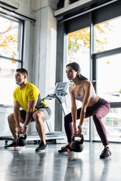 sportsman and sportswoman doing squat with weights in sports center